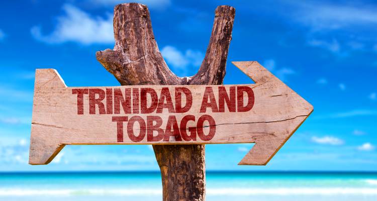 Panneau en bois en forme de flèche indiquant « Trinité-et-Tobago » pointant vers une mer turquoise et un ciel bleu.