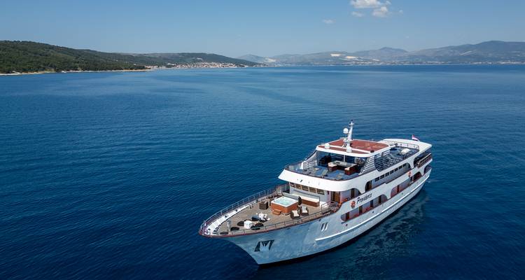 Vista aérea de un yate de crucero boutique atravesando aguas azul cobalto cerca de colinas ondulantes de Croacia.