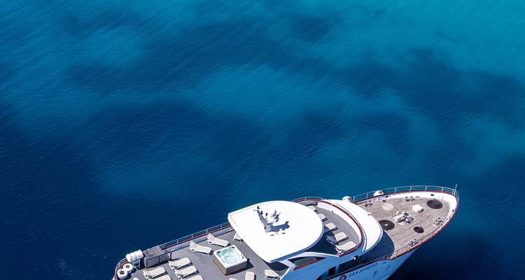 Vista aérea parcial de la proa del yate sobre un mar azul vibrante que muestra gradientes de color del agua.
