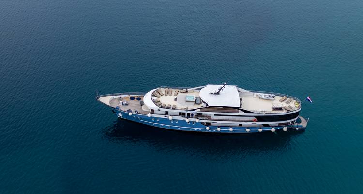 Vue aérienne oblique d'un yacht de luxe à coque bleue flottant sur une mer turquoise calme