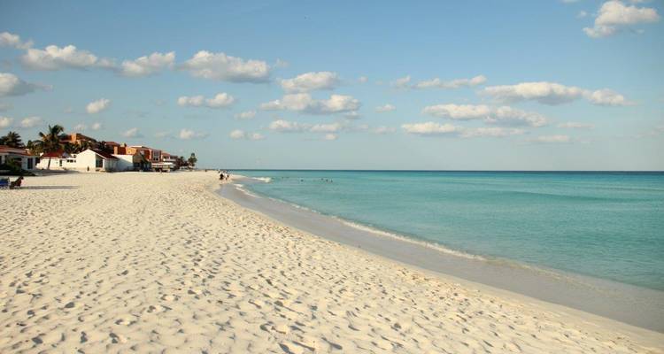 Brede strook wit zandstrand omgeven door turquoise Caribisch water onder een gespikkelde hemel.