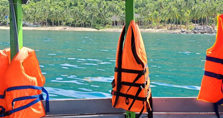 Bright orange life jackets hanging on a small boat with turquoise water and palm-fringed shore behind.