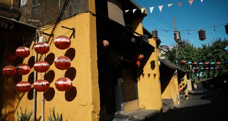 Shadowed yellow alley with rows of red lanterns and festive buntings in late afternoon light.