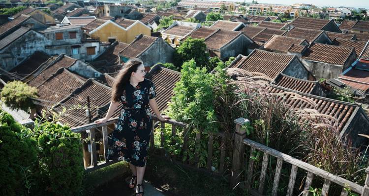 Female traveler in floral dress admiring panoramic rooftop view of tiled houses.