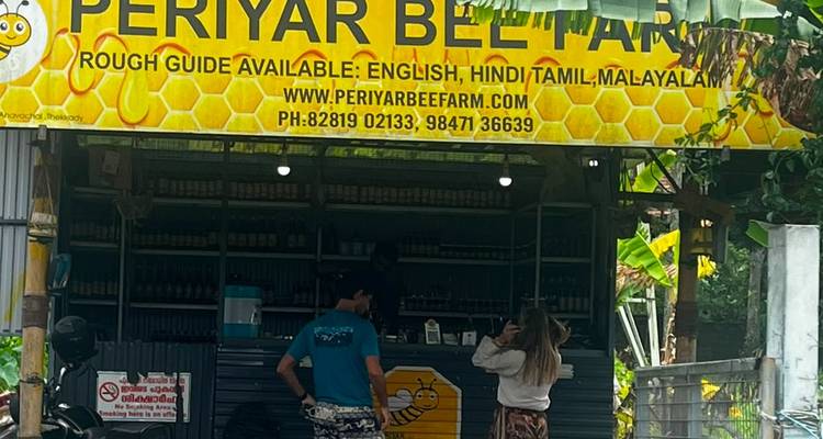 Kleine Ladenfront einer Periyar Bee Farm am Straßenrand mit Wabenschild und Kunden beim Stöbern.