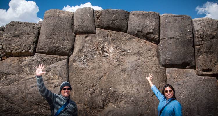 Deux touristes lèvent les mains contre les gigantesques blocs de pierre ajustée de la forteresse de Saqsaywaman.