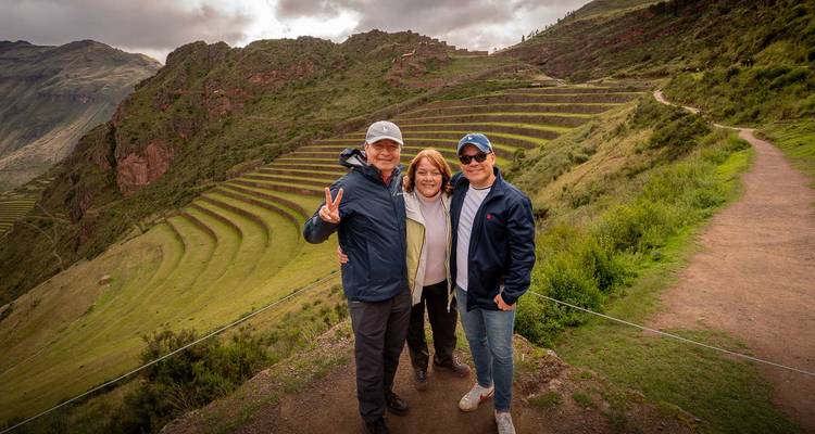 Trois voyageurs posent en souriant devant les terrasses agricoles de Pisac dans la Vallée Sacrée.