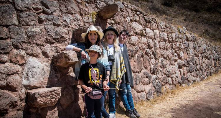 Un groupe familial pose à côté d'un mur de pierre inca ancien sous un soleil éclatant.