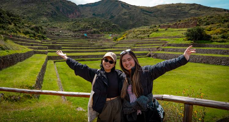 Deux amis aux bras écartés souriants devant des terrasses agricoles luxuriantes et verdoyantes dans les Andes.
