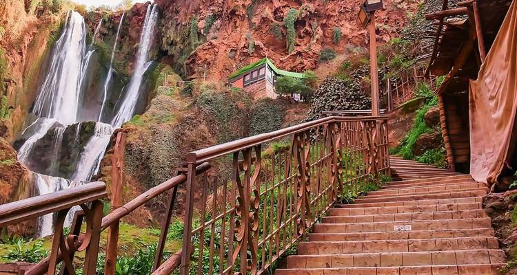 Escalera empinada con azulejos y barandilla de hierro que lleva hacia paredes de cañón rojo y una cascada