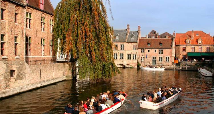 Les bateaux de tourisme naviguent dans un canal tranquille bordé de bâtiments médiévaux en brique à Bruges.