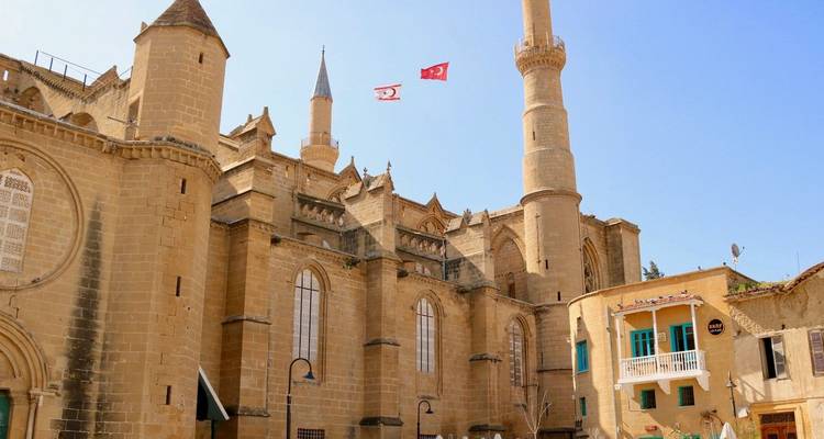 Historische zandstenen moskee-kathedraal met minaret en Turkse vlaggen tegen een heldere blauwe lucht.
