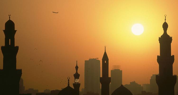 Minaretes recortados contra el cielo y el horizonte de la ciudad de El Cairo en la puesta de sol dorada con un avión en el cielo.