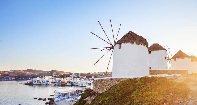 Iconische witte windmolens die uitkijken over de blauwe baai en het stadje Mykonos bij gouden zonsopgang.