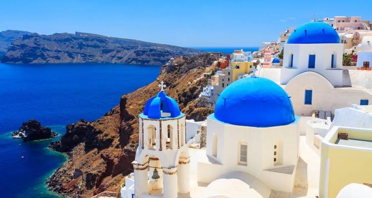 Klassische Aussicht auf die blaudomigen Kirchen von Oia, die über dem tiefblauen Ägäischen Meer leuchten.