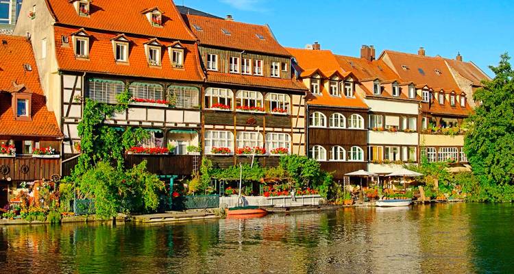 Farbenfrohe Fachwerkhauser am Fluss in Bamberg mit Spiegelungen im ruhigen Wasser.