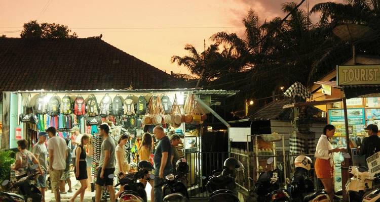 Ein abendlicher Straßenmarkt summt vor Käufern zwischen Rollern und hell beleuchteten Ständen.