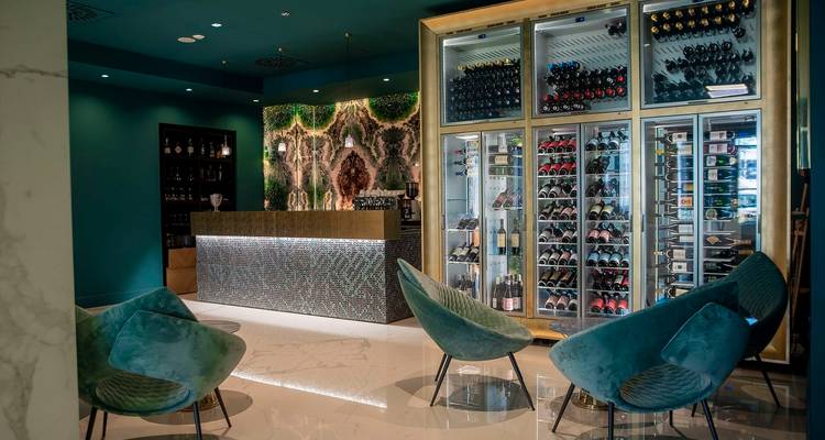 Stijlvolle hotelbar met turquoise muren, fluwelen stoelen en wijnkasten van vloer tot plafond.