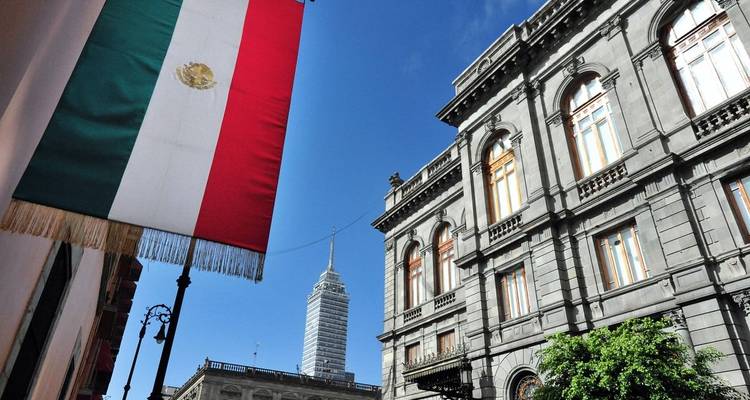 Mexikanische Flagge, die neben historischen Gebäuden in Mexiko-Stadt mit dem Torre Latinoamericana im Hintergrund weht.
