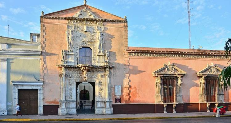 Historische Kolonialfassade in Merida mit Passanten gegen blauen Morgenhimmel.
