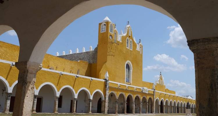 Helles gelbes Kloster von Izamal, gerahmt von Steinbögen unter blauem Himmel.