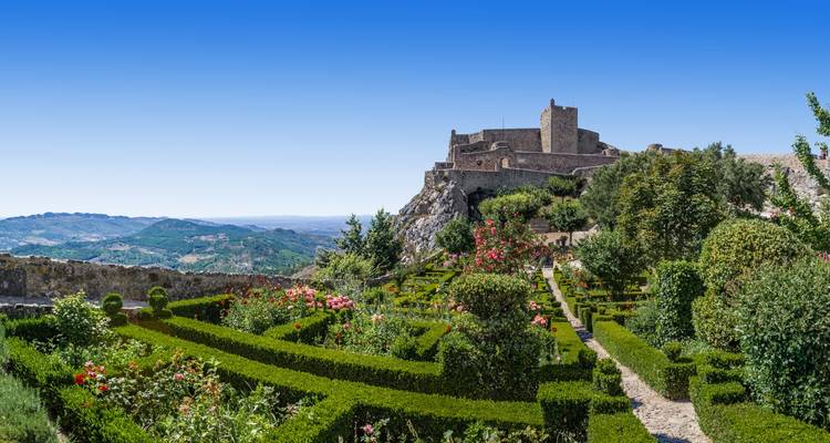 Forteresse de pierre au sommet de la colline dominant des jardins en terrasse formels avec des fleurs éclatantes et des haies de buis