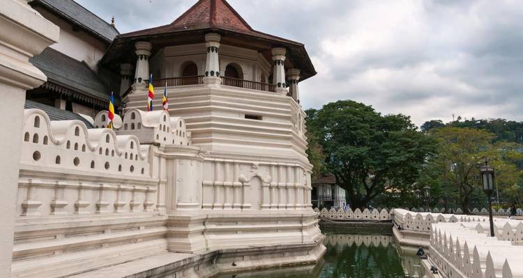 Complejo del Templo de la Reliquia del Diente de paredes blancas reflejado en un foso bajo un cielo nublado en Kandy.
