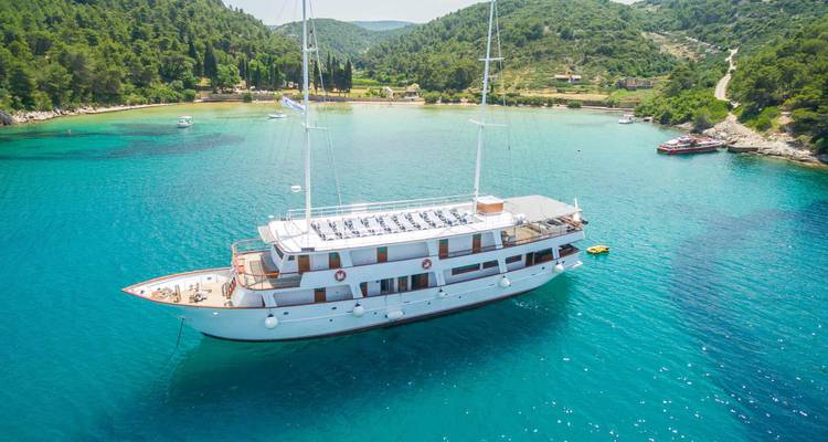 Een strak wit jacht afgemeerd in een afgelegen turquoise baai omgeven door met dennen begroeide heuvels in Kroatië.