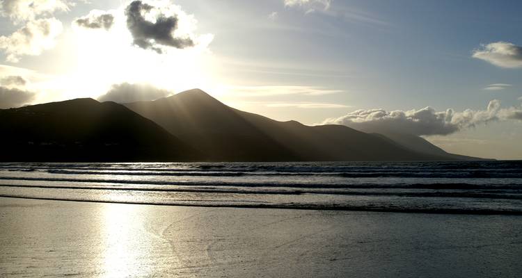 Les rayons de soleil percent les nuages au-dessus des montagnes côtières et des vagues réfléchissantes au crépuscule.