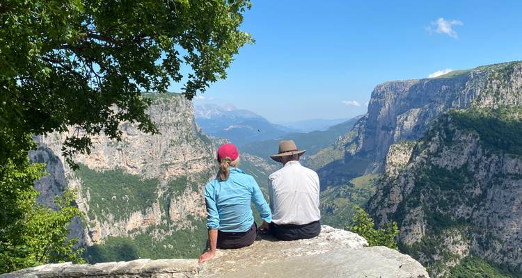 Twee wandelaars zitten op een rotsachtige richel met uitzicht op de dramatische rotswanden en valleien van Vikos Gorge.
