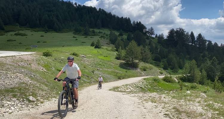 Wielrenners rijden op e-bikes een grind bergweg op onder een heldere zomerse hemel.