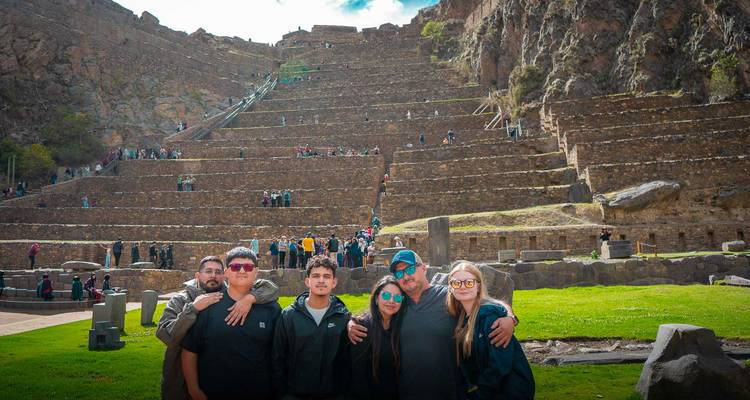 Grupo de amigos posando brazo a brazo frente a las empinadas terrazas de piedra de la fortaleza de Ollantaytambo en el Valle Sagrado de Perú.