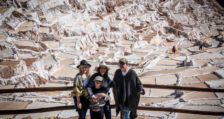 La familia posa ante el mosaico de brillantes salinas blancas de Maras bajo la luminosa luz andina.