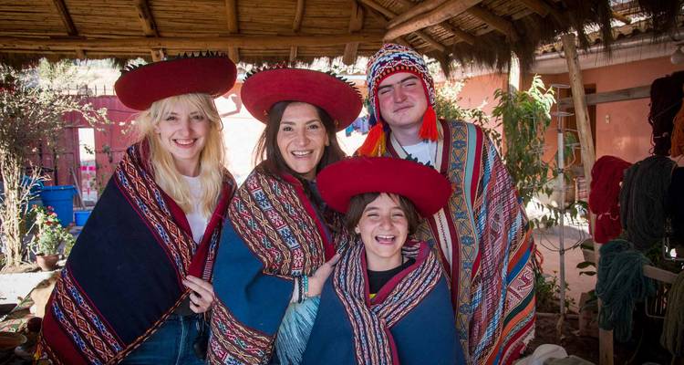 Visitantes sonrientes vestidos con coloridos textiles tradicionales andinos dentro de un taller de tejido.