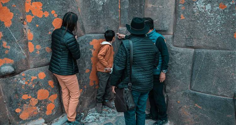 Los viajeros examinan las juntas de piedra precisas de un muro inca cubierto con líquenes anaranjados.