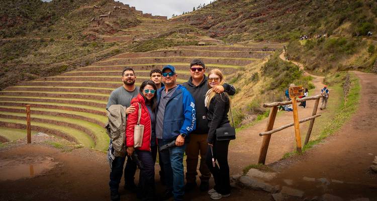 Foto grupal en un camino de tierra que da vista a las terrazas escalonadas de Pisac con colinas escarpadas de fondo.