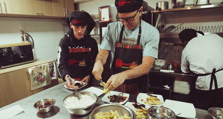 Los participantes sirven arroz y papas fritas durante una clase de cocina peruana, usando delantales y sombreros de chef a juego.