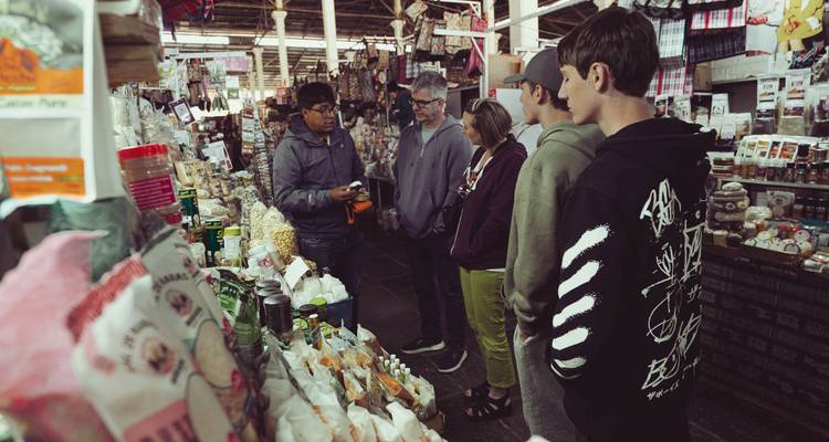 Un pequeño grupo de turistas escucha a un guía local entre los puestos abarrotados de especias, granos y productos frescos en el Mercado San Pedro de Cusco.