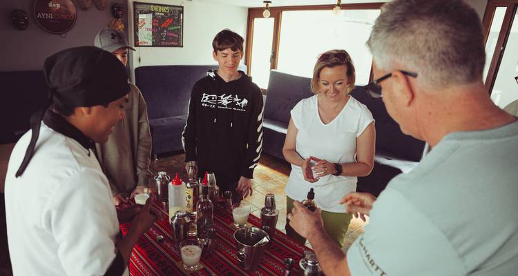 Un pequeño grupo en una sala acogedora aprendiendo a mezclar bebidas con un chef e ingredientes sobre una mesa.