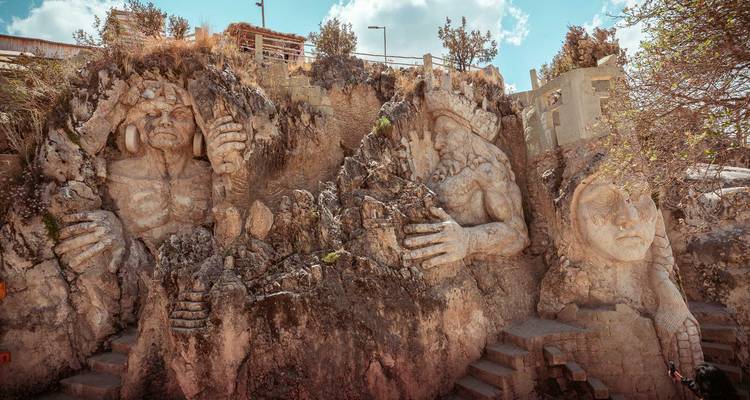 Serie de colosales esculturas de piedra de figuras mitológicas incrustadas en la cara de un acantilado.