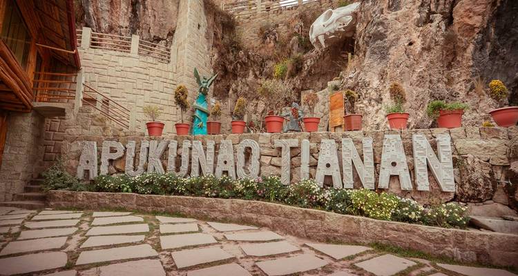 Patio de piedra con letras grandes que forman APUKUNAO TIANAN contra una pared de roca.