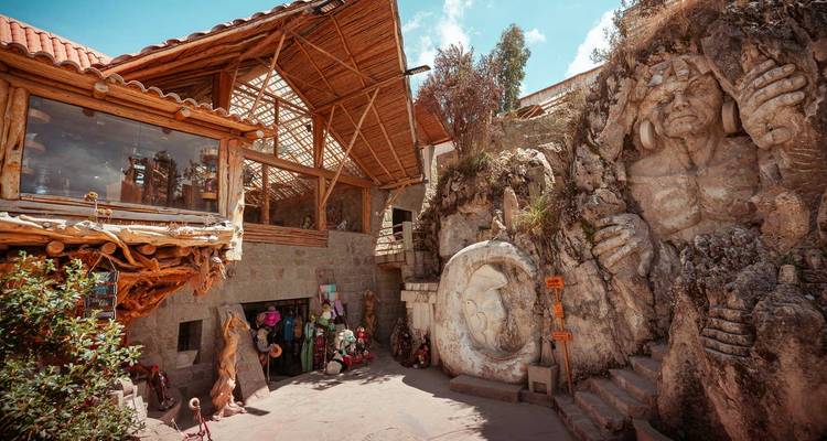 Complejo rústico con estructuras de madera junto a figuras de piedra tallada y cielo brillante arriba.