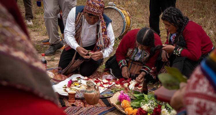 Ceremonia andina de cerca: chamán prepara pétalos de flores y hojas de coca sobre telas coloridas.