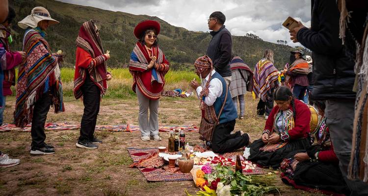 Los participantes con ponchos vibrantes se reúnen alrededor de un chamán arrodillado durante un ritual al aire libre.