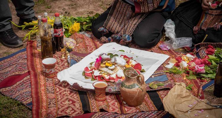 Vista cercana de una ofrenda ceremonial con pétalos, hojas de coca y chicha sobre un paño con patrones.