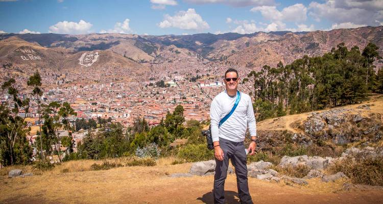 El viajero posa frente a la vista panorámica de los techos de terracota de Cusco y las colinas circundantes.