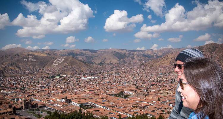 Dos viajeros sonríen mientras admiran la vista panorámica de Cusco bajo unas nubes esponjosas.
