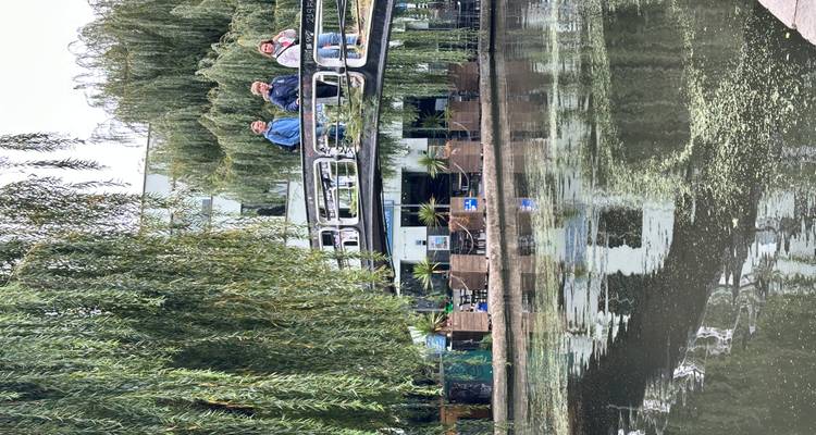 Rustig kanaallandschap met treurwilgen en drie mensen die een boogbrug oversteken.