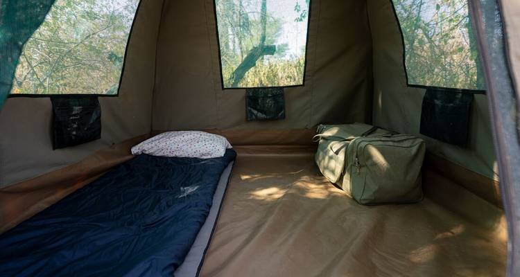 Intérieur d'une simple tente de safari en toile avec un sac de couchage et un sac de voyage posés sur le sol.
