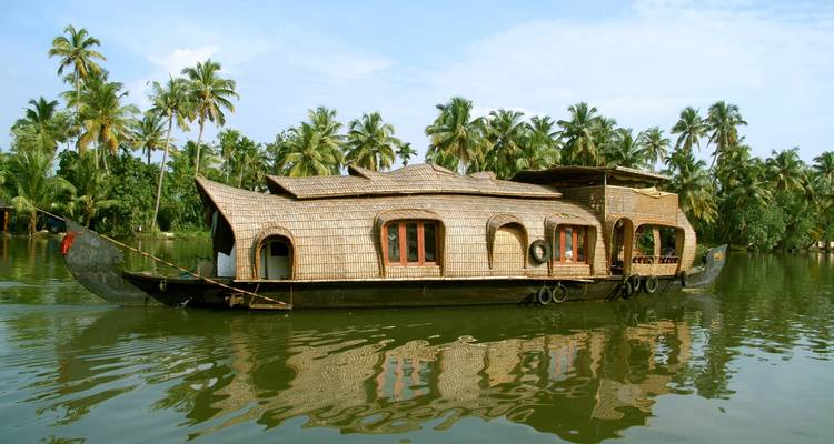Casa flotante de madera tradicional flotando en aguas tranquilas rodeada de altos cocoteros.